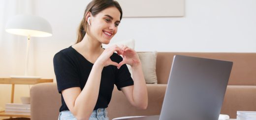 Tietokoneella istuu nainen, jolla kädet muodostavat sydämen.
