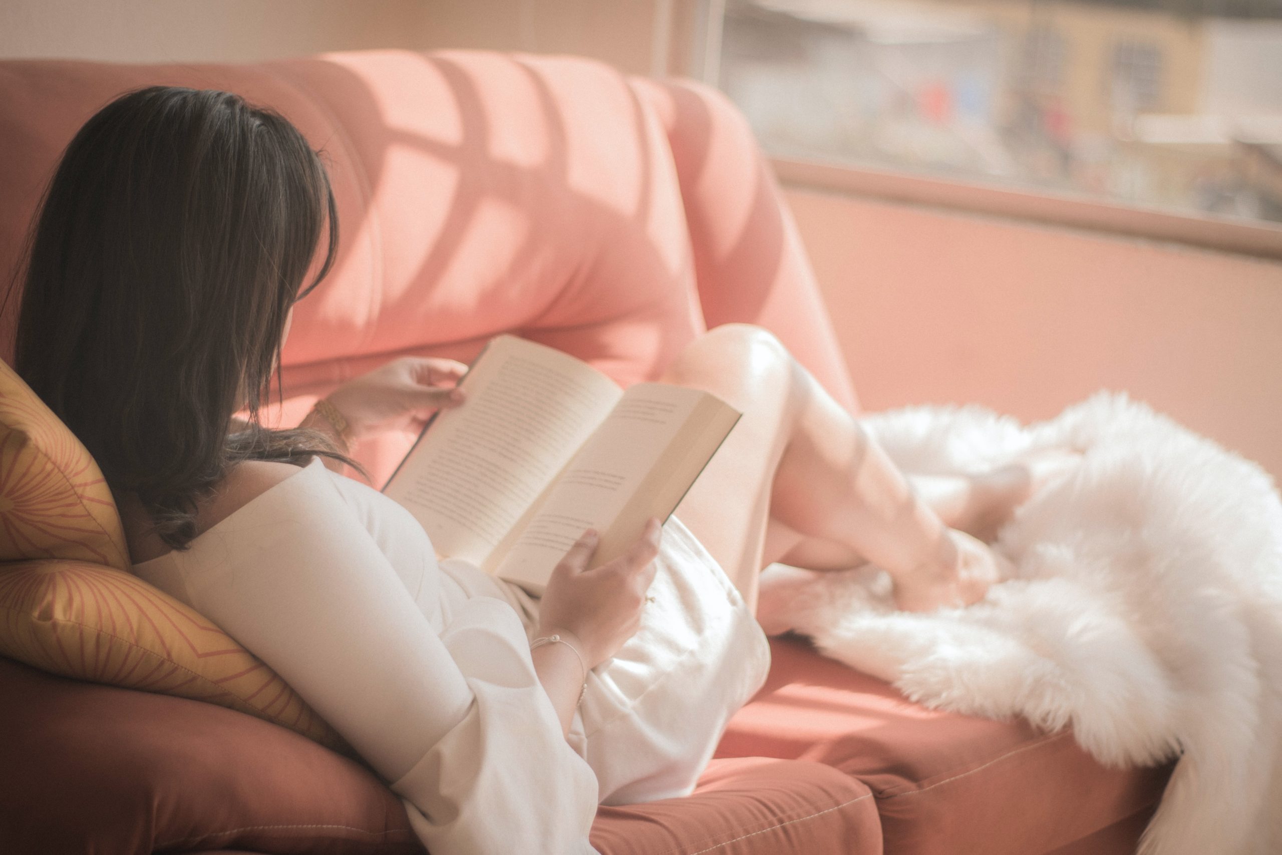 Nainen lukee kirjaa sohvalla.
