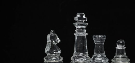 Neljä lasista shakkinappulaa mustaa taustaa vasten.