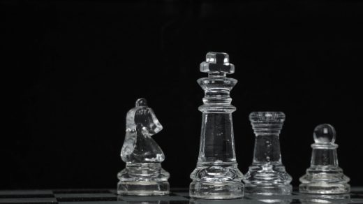 Neljä lasista shakkinappulaa mustaa taustaa vasten.